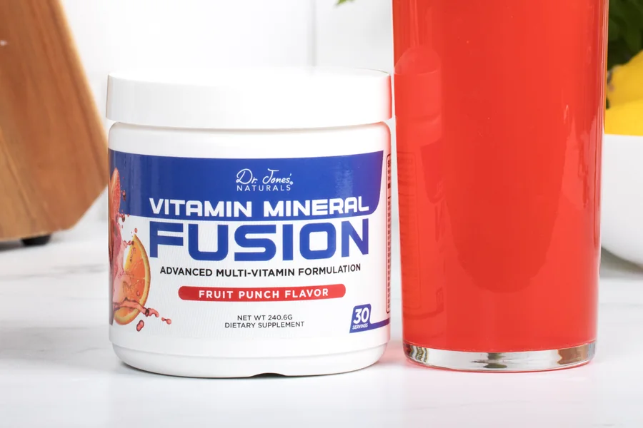 Vitamin Mineral Fusion tub next to a tall glass of the red fruit punch drink on a kitchen counter