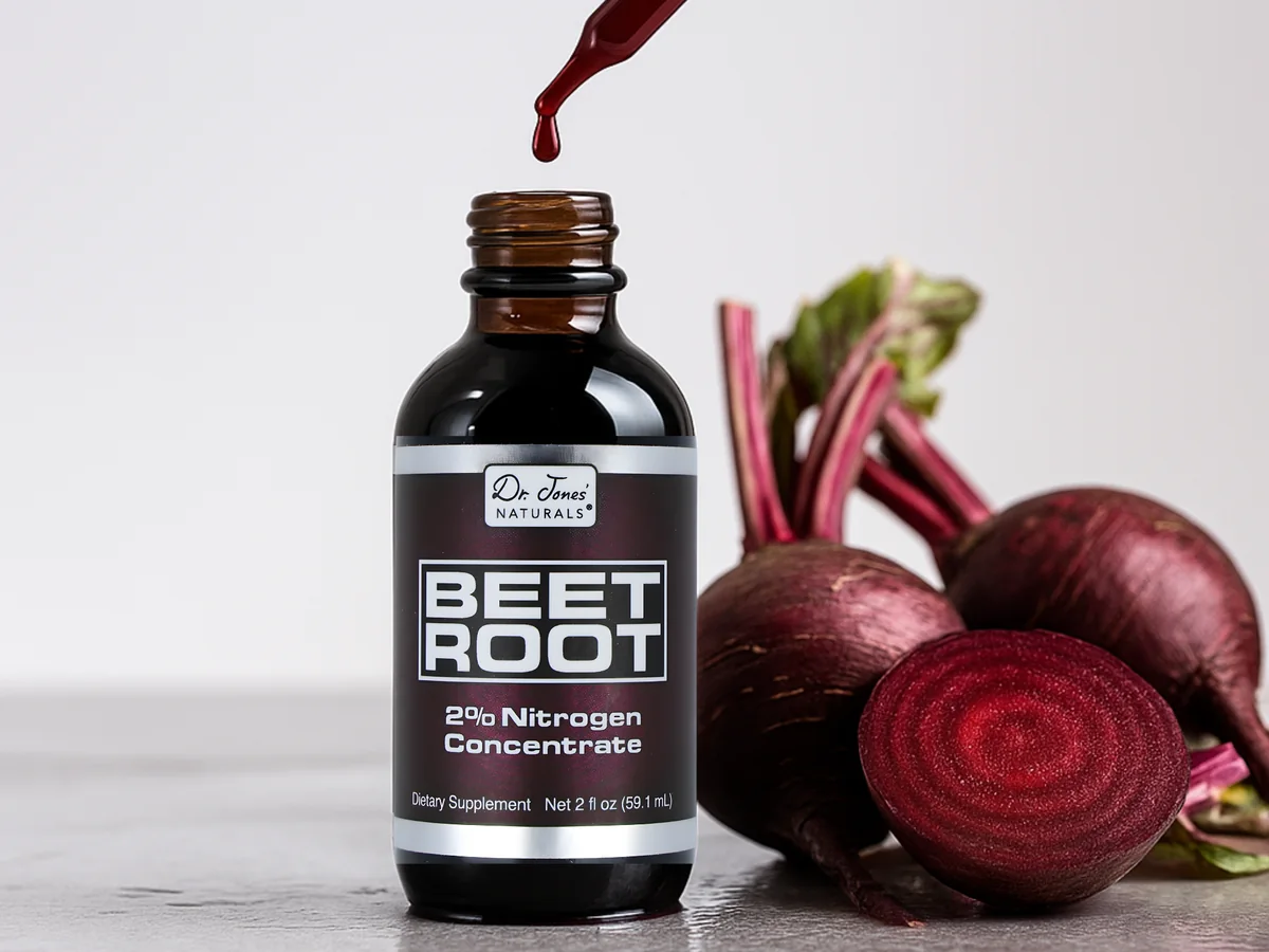 A dropper releases a drop of red beet concentrate into the Beetroot Concentrate bottle beside fresh beets