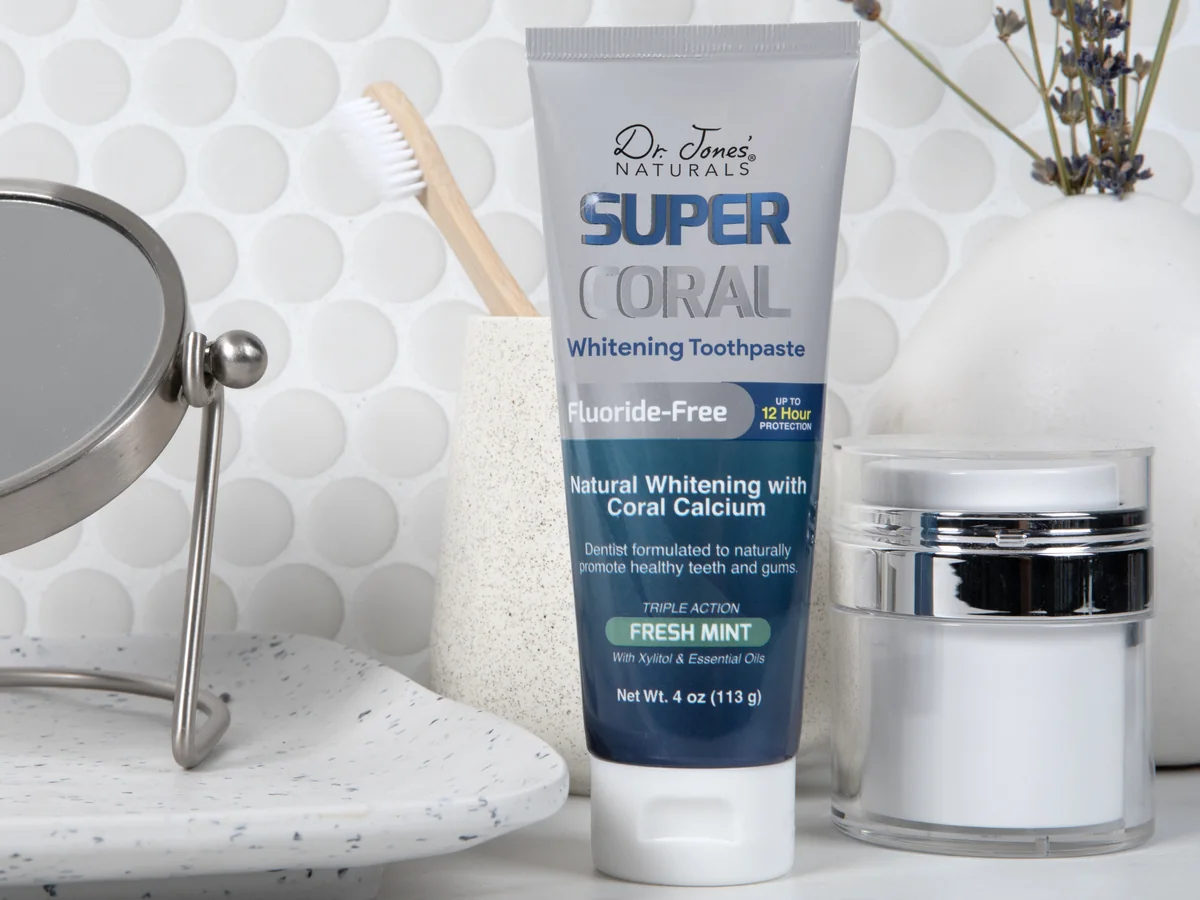 Super Coral Whitening Toothpaste on a bathroom counter beside a toothbrush cup and a round mirror