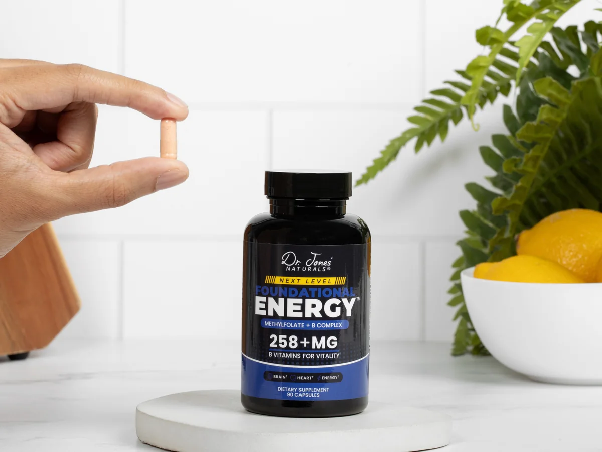 A hand holds one Next Level capsule above the bottle on a white kitchen counter
