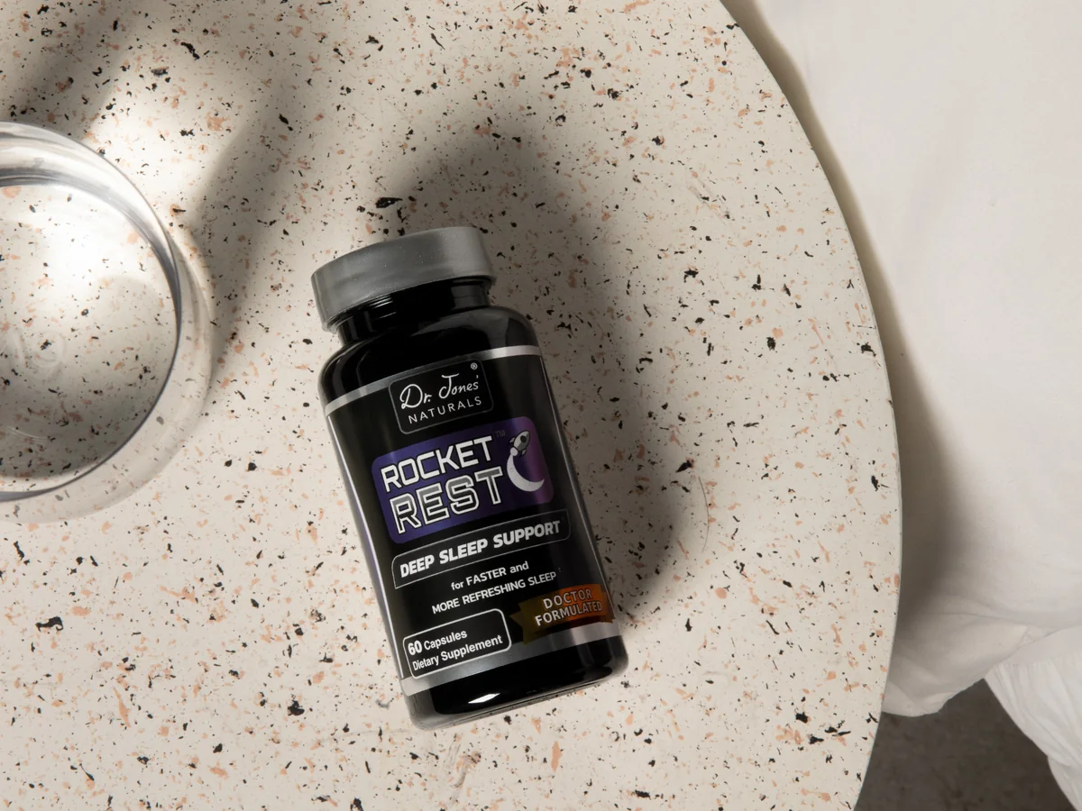 A bottle of Rocket Rest Plus lying on a speckled stone tray beside a glass