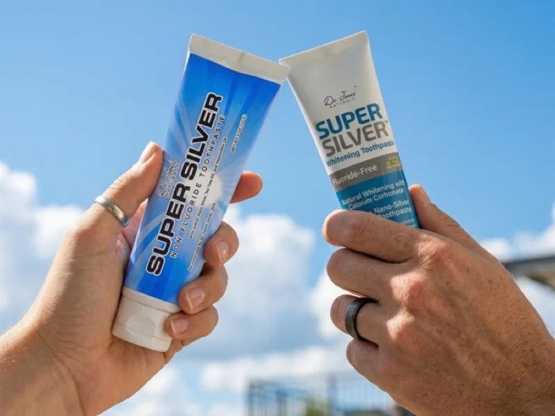 Two hands raise tubes of SuperSilver toothpaste against a blue sky