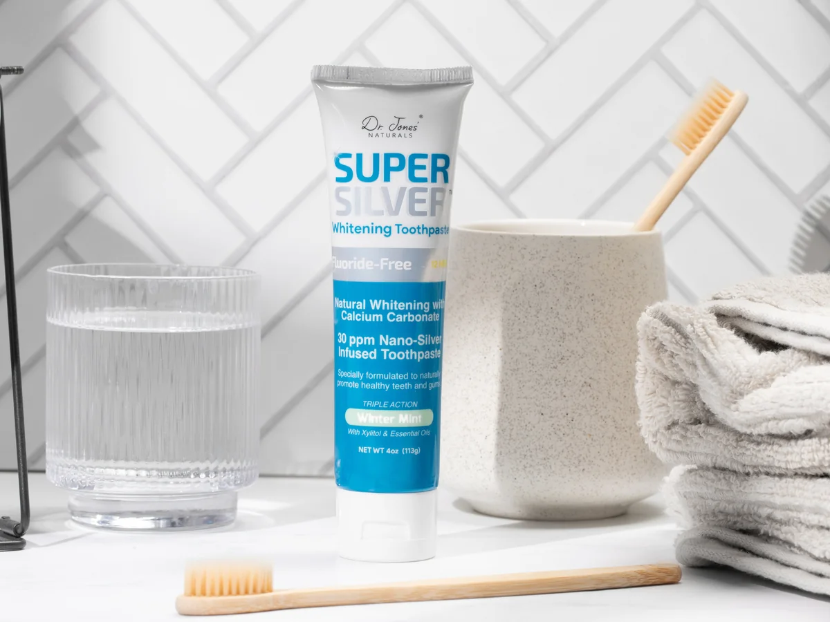 SuperSilver Whitening Toothpaste on a bathroom counter with a glass of water and a bamboo toothbrush