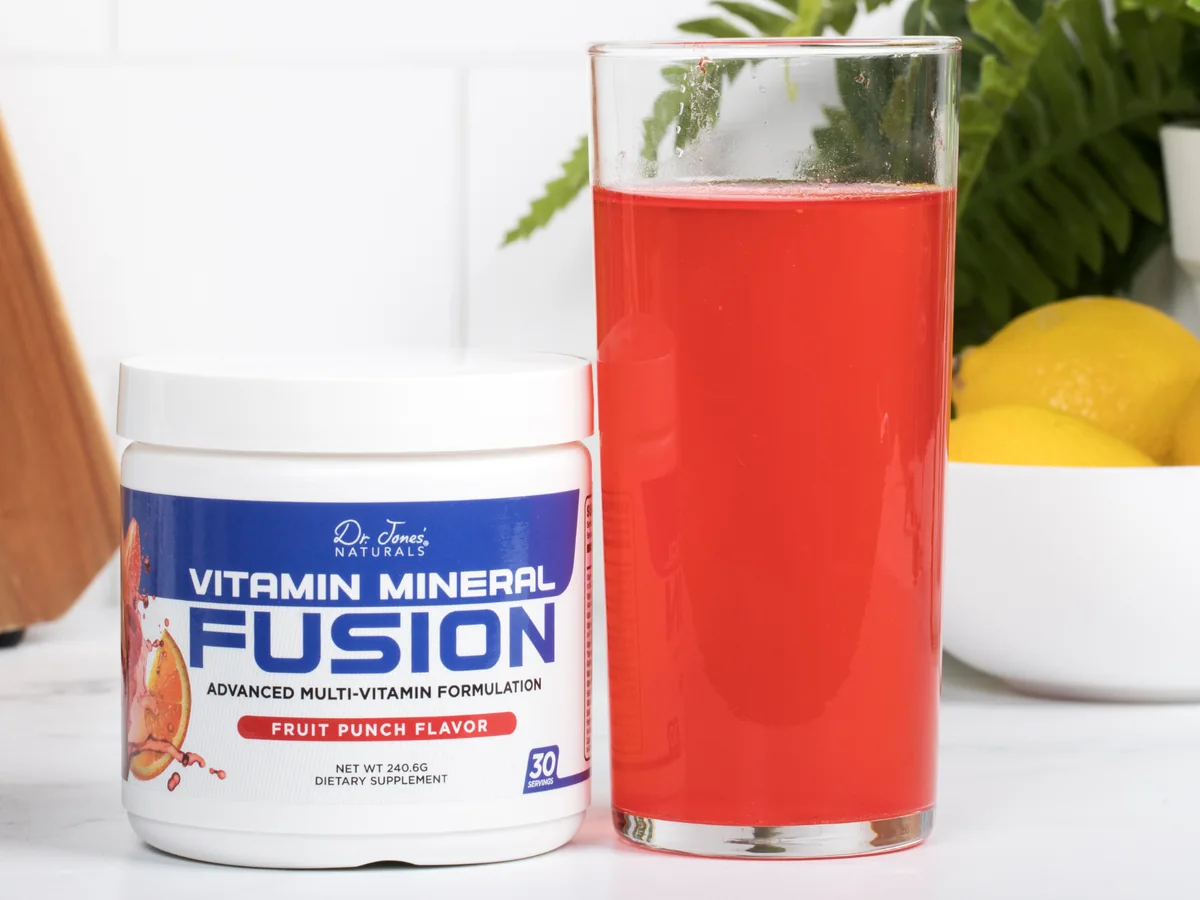 Vitamin Mineral Fusion tub and a tall glass of the red fruit punch drink on a kitchen counter